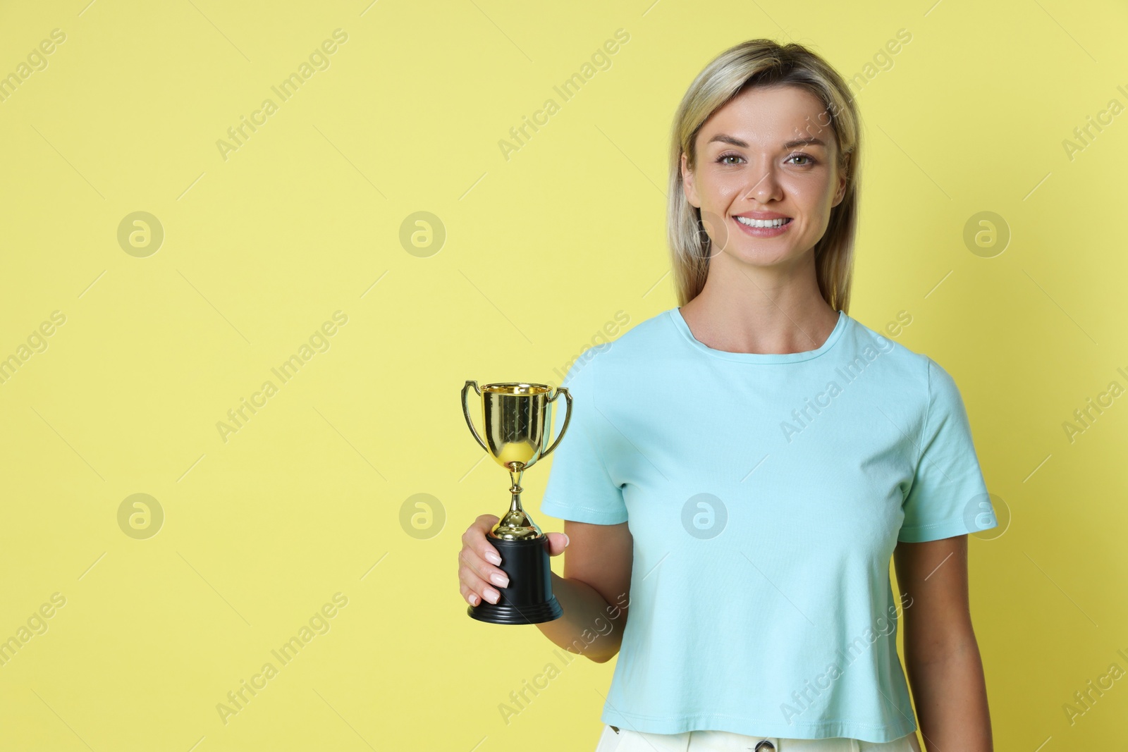 Photo of Happy winner with golden trophy cup on yellow background, space for text