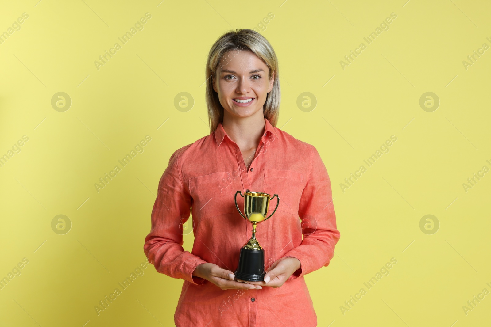 Photo of Happy winner with golden trophy cup on yellow background