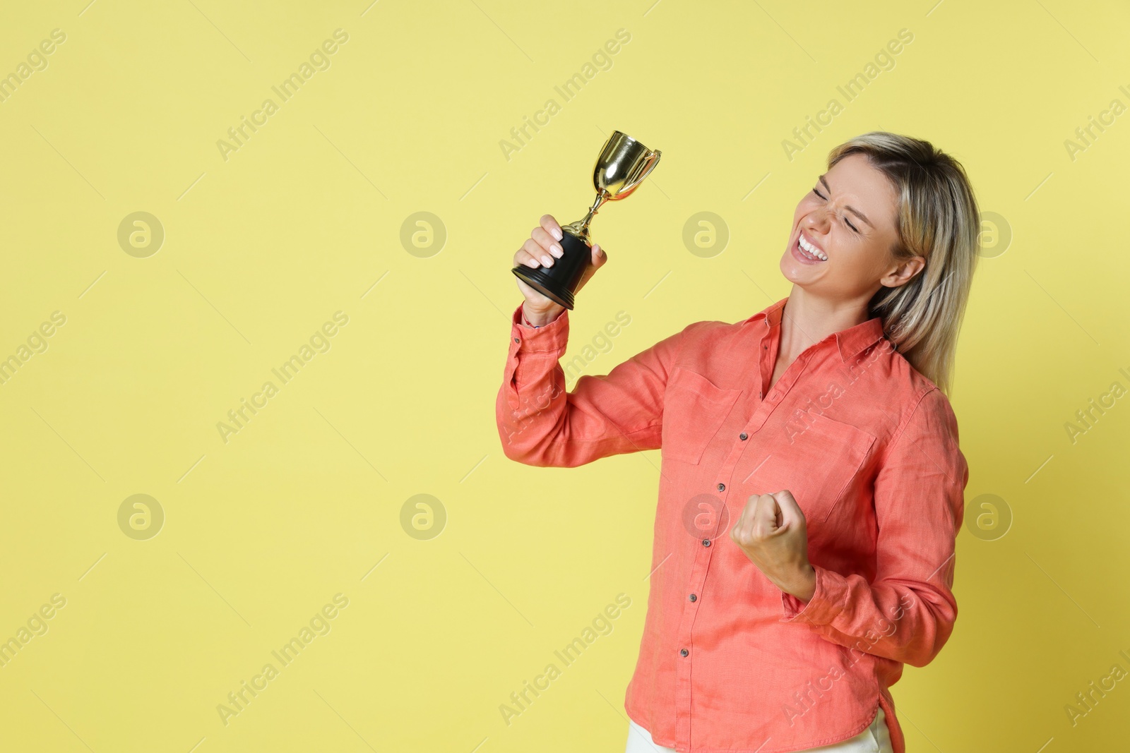 Photo of Happy winner with golden trophy cup on yellow background, space for text