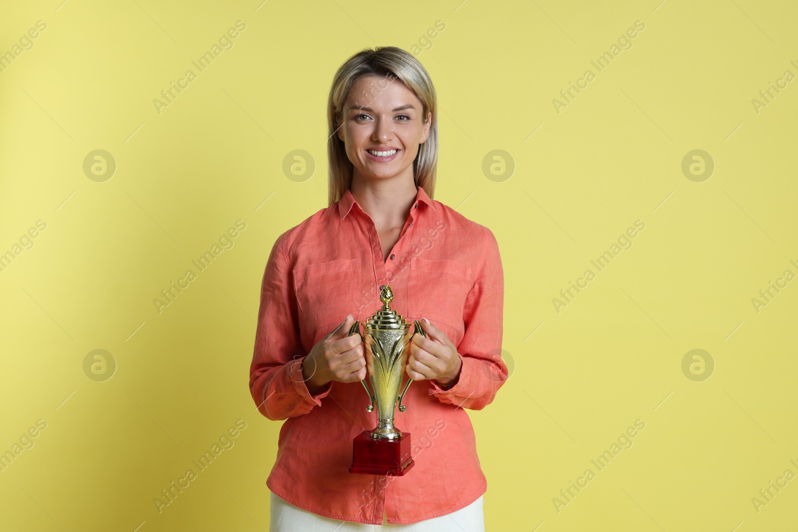 Photo of Happy winner with golden trophy cup on yellow background