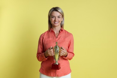 Photo of Happy winner with golden trophy cup on yellow background