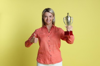 Photo of Happy winner with golden trophy cup showing thumbs up on yellow background