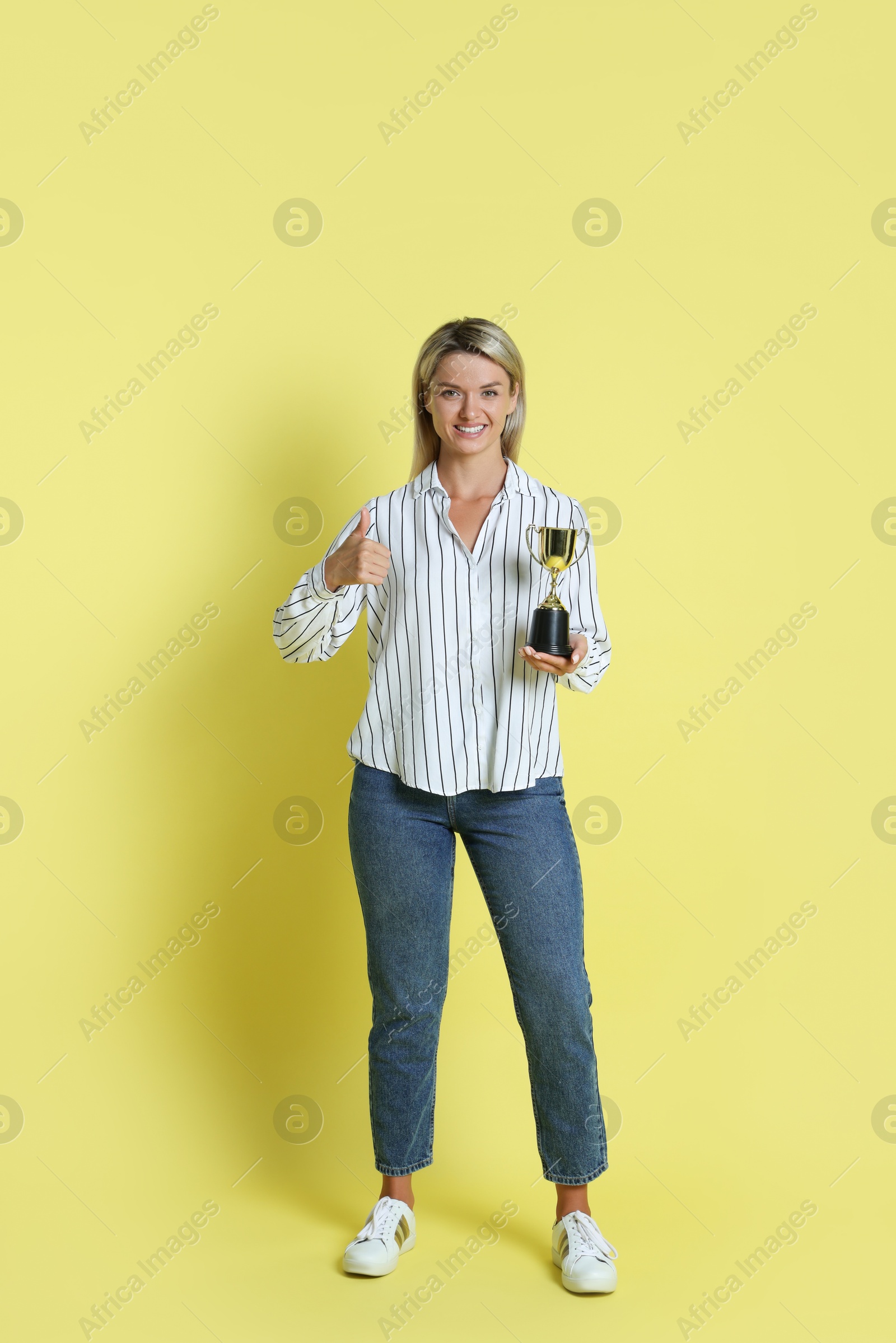 Photo of Happy winner with golden trophy cup on yellow background