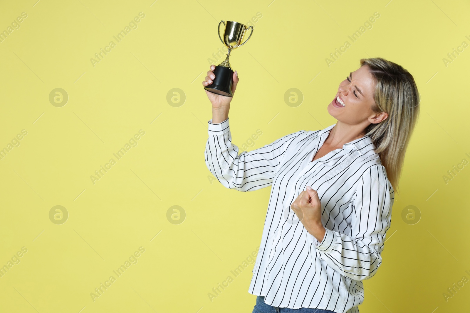 Photo of Happy winner with golden trophy cup on yellow background, space for text