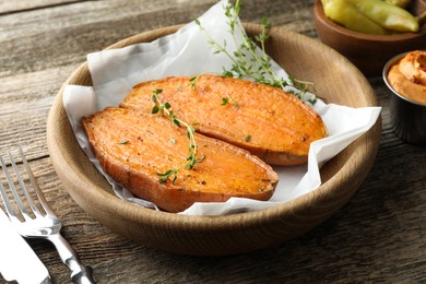 Photo of Tasty cooked sweet potato served with thyme on wooden table, closeup