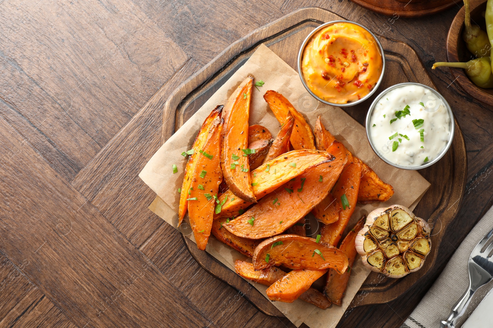 Photo of Tasty cooked sweet potatoes served with sauces on wooden table, top view. Space for text