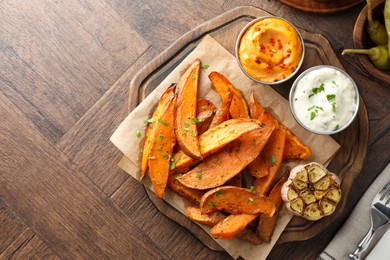 Tasty cooked sweet potatoes served with sauces on wooden table, top view. Space for text