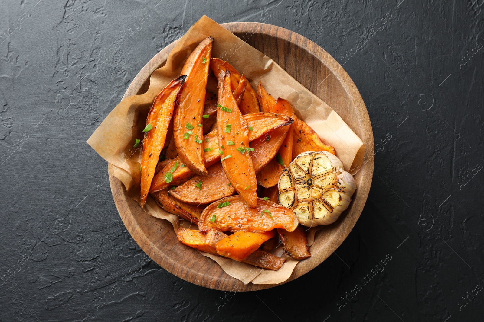 Photo of Tasty cooked sweet potatoes with parsley and garlic on black table, top view