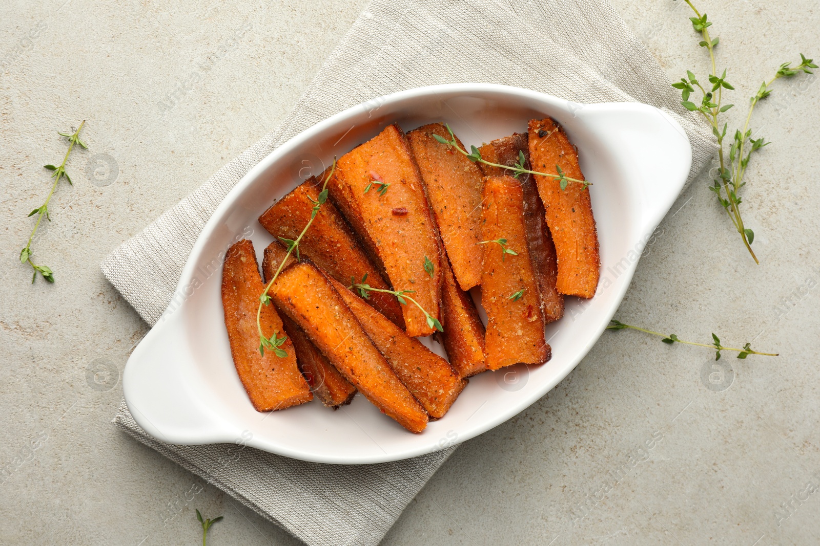 Photo of Pieces of tasty cooked sweet potato in baking dish with microgreens on light textured table, top view