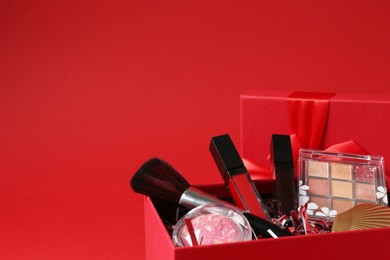 Photo of Christmas gift box with cosmetic products on red background, closeup. Space for text