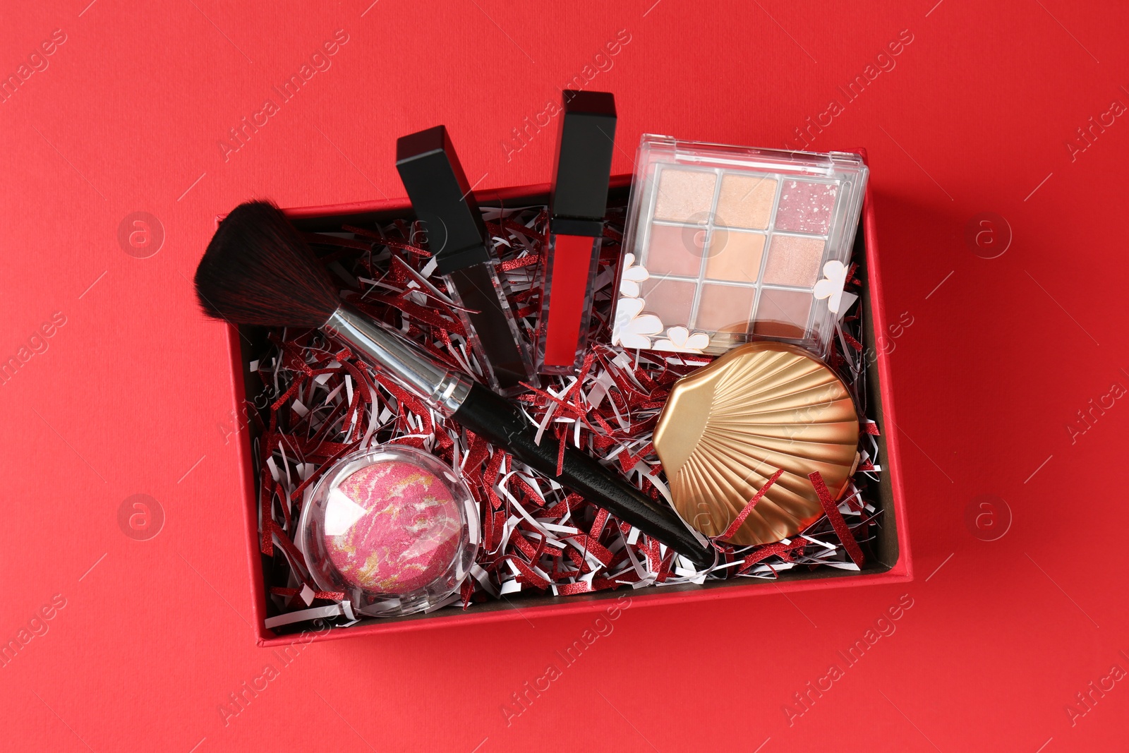 Photo of Christmas gift box with cosmetic products on red background, top view