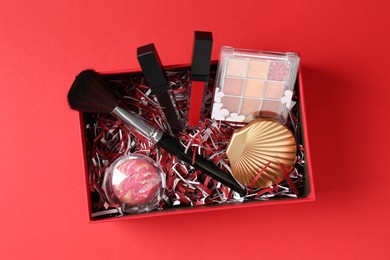 Photo of Christmas gift box with cosmetic products on red background, top view