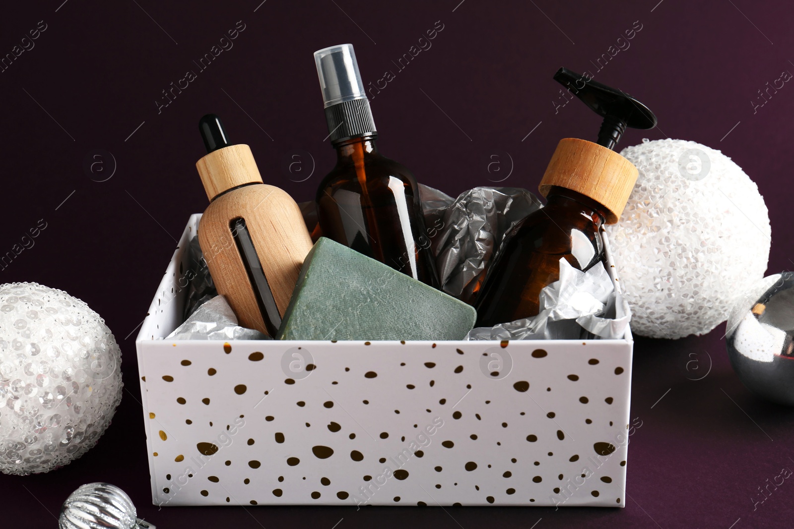 Photo of Cosmetic products in box as Christmas gift and festive balls on black background