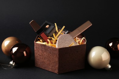 Photo of Gift box with decorative cosmetics and Christmas balls on black background