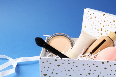 Photo of Cosmetic products in gift box on blue background, closeup. Space for text