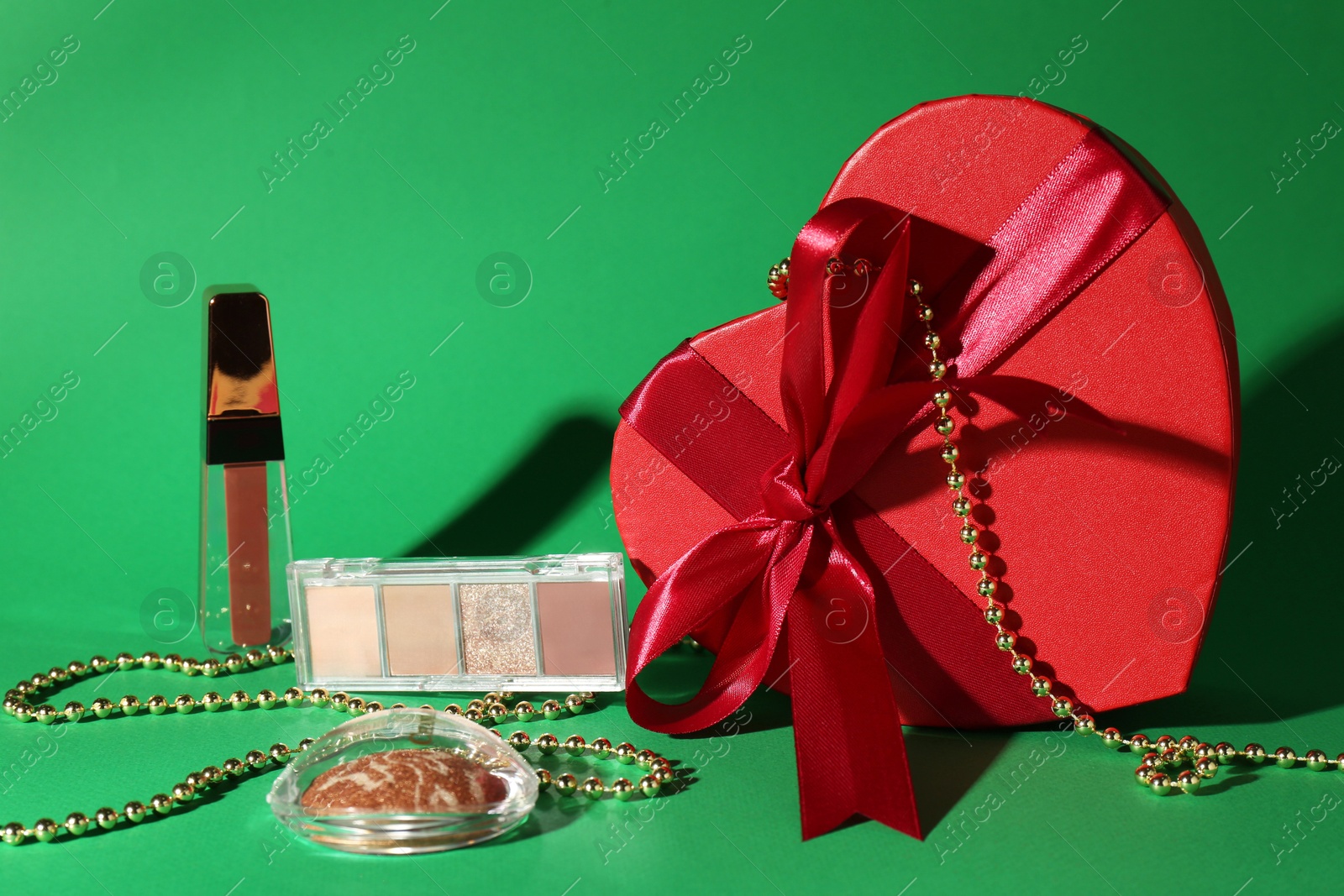 Photo of Christmas present with decorative cosmetics and red gift box on green background