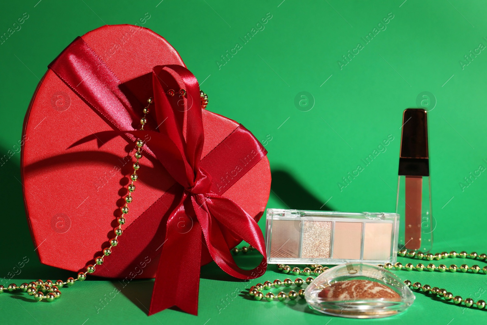 Photo of Christmas present with decorative cosmetics and red gift box on green background