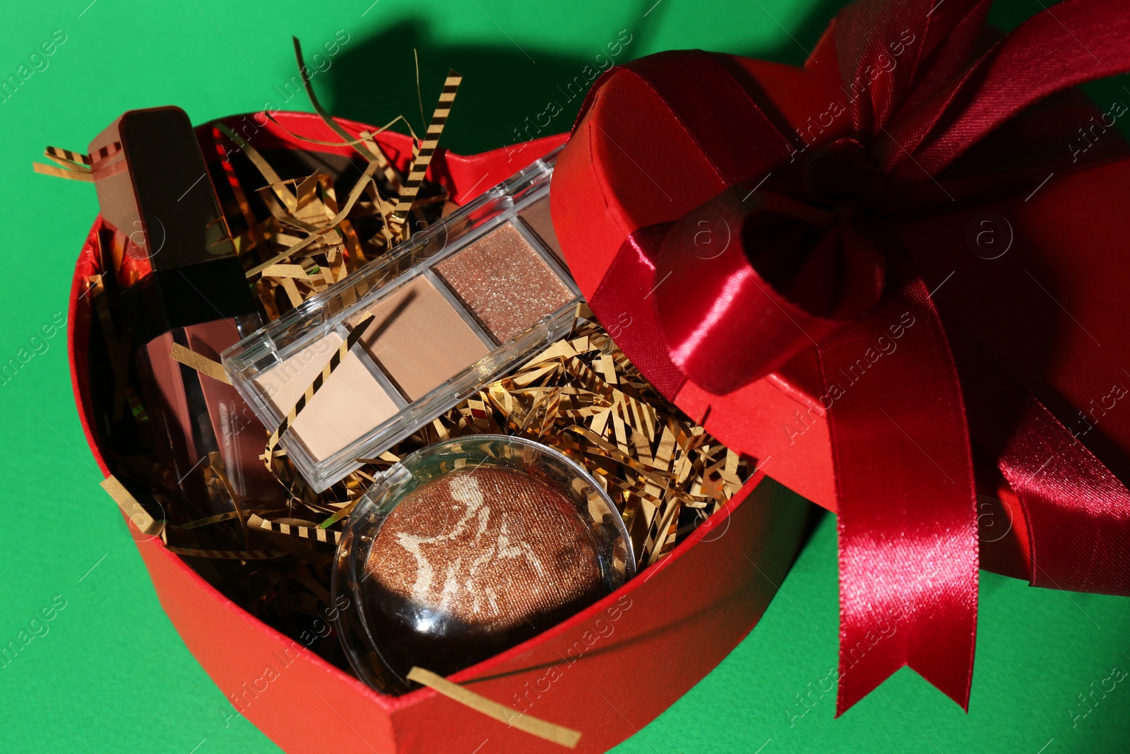 Photo of Christmas gift box with decorative cosmetics on green background, closeup