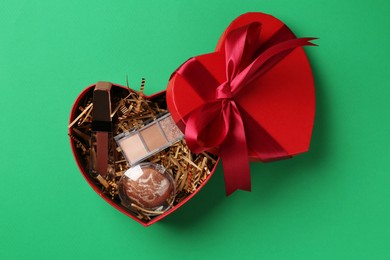 Photo of Christmas gift box with decorative cosmetics on green background, top view. Space for text