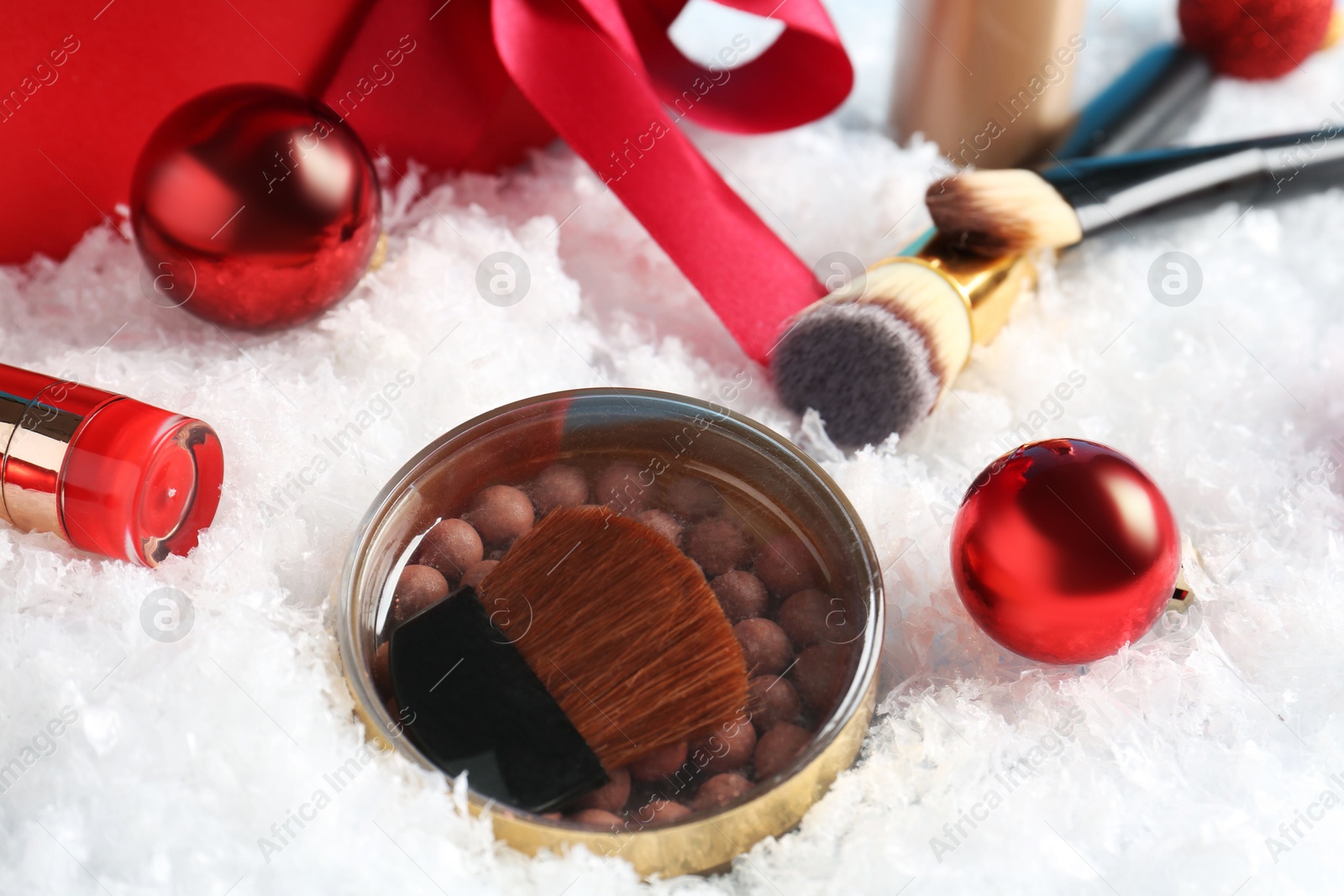 Photo of Christmas present. Decorative cosmetics and makeup brushes on snow, closeup