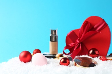 Photo of Christmas present. Decorative cosmetics and gift box on snow against light blue background. Space for text