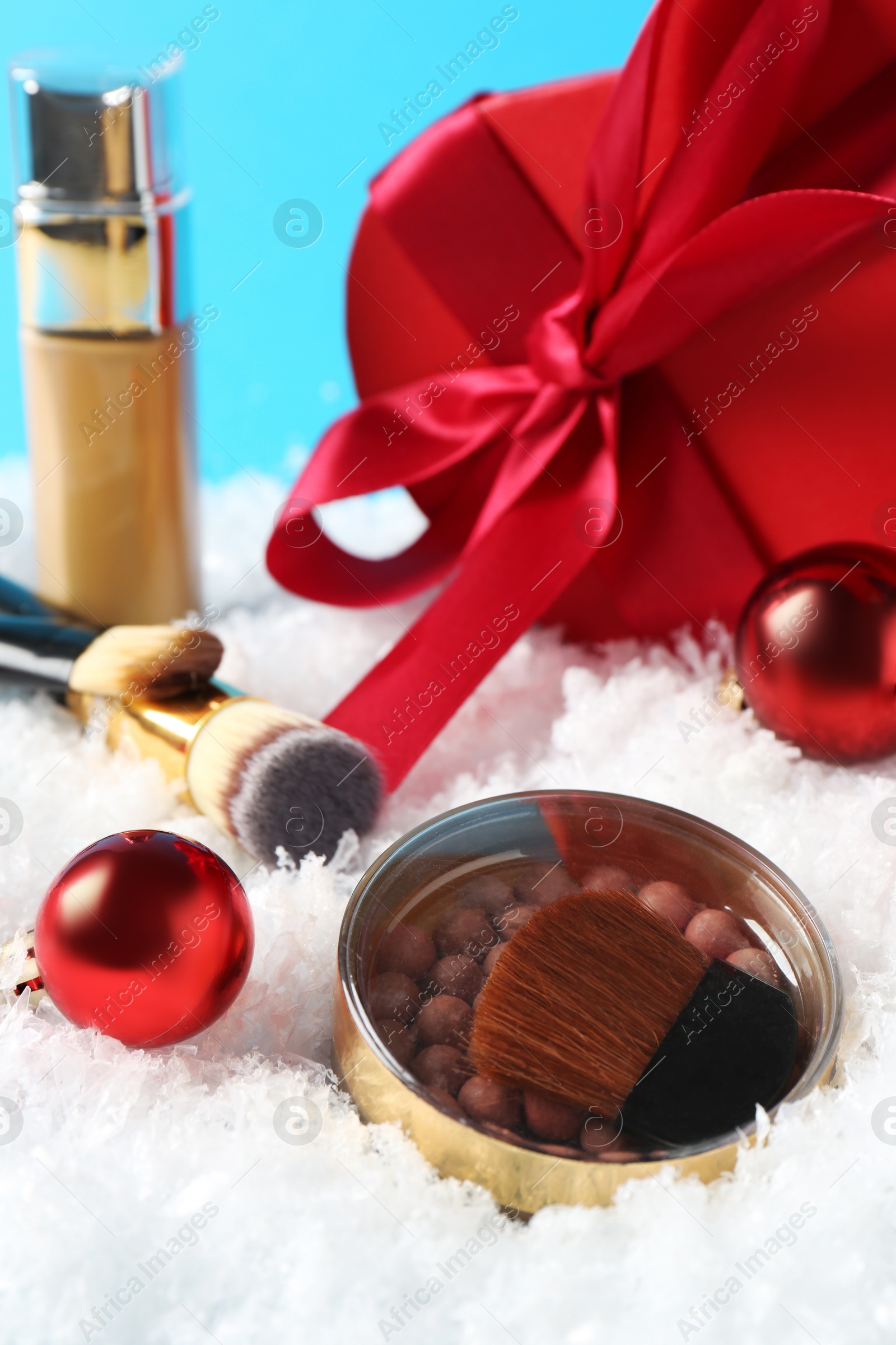 Photo of Christmas present. Decorative cosmetics and gift box on snow against light blue background, closeup