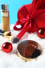 Christmas present. Decorative cosmetics and gift box on snow against light blue background, closeup