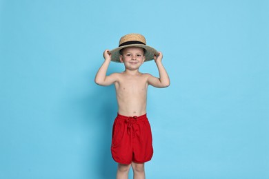 Photo of Cute little boy in beachwear with straw hat on light blue background