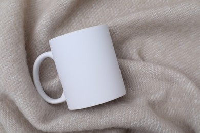 Photo of Blank white ceramic mug on beige fabric, top view. Mockup for design