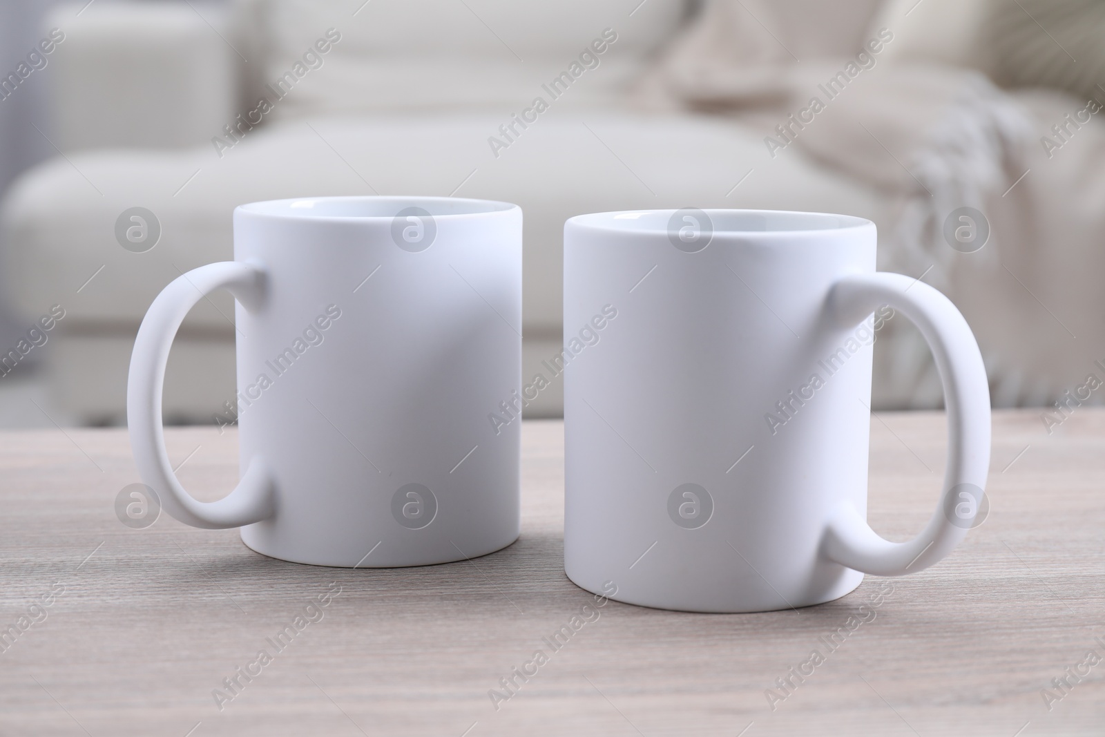 Photo of Blank ceramic mugs on white wooden table. Mockup for design