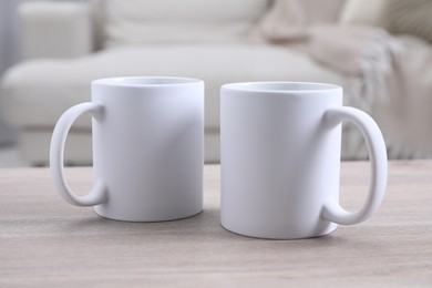 Photo of Blank ceramic mugs on white wooden table. Mockup for design