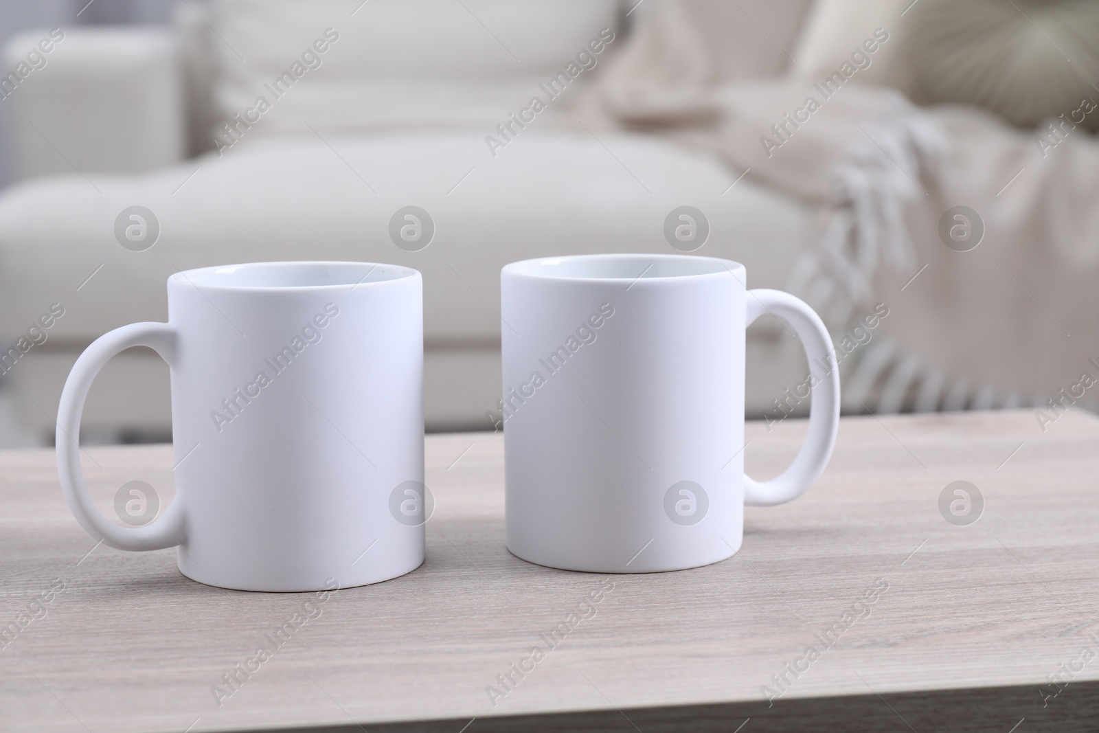 Photo of Blank ceramic mugs on white wooden table. Mockup for design