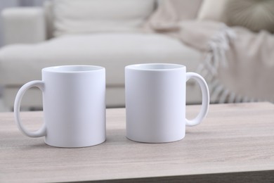 Photo of Blank ceramic mugs on white wooden table. Mockup for design