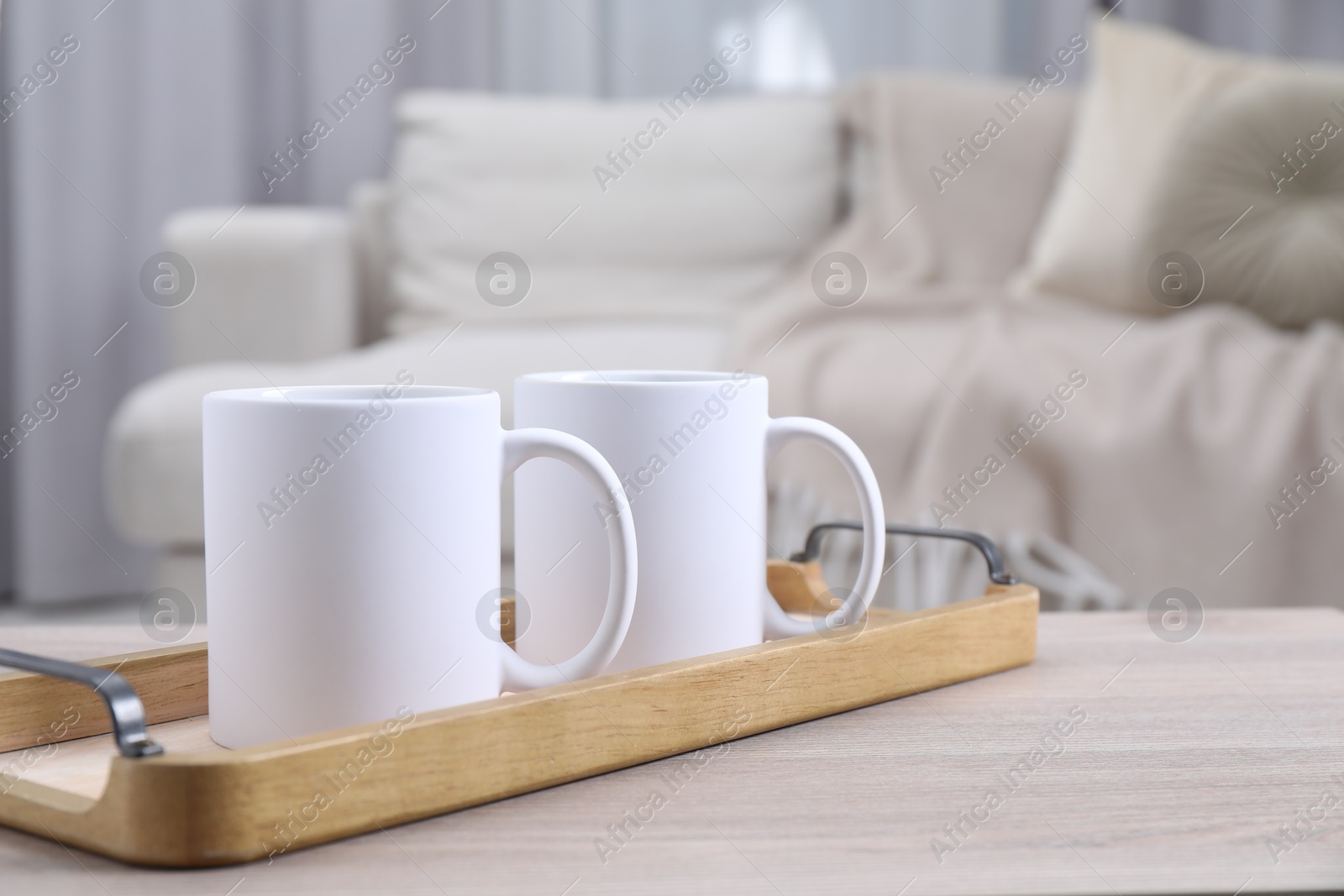 Photo of Blank ceramic mugs on white wooden table indoors. Mockup for design