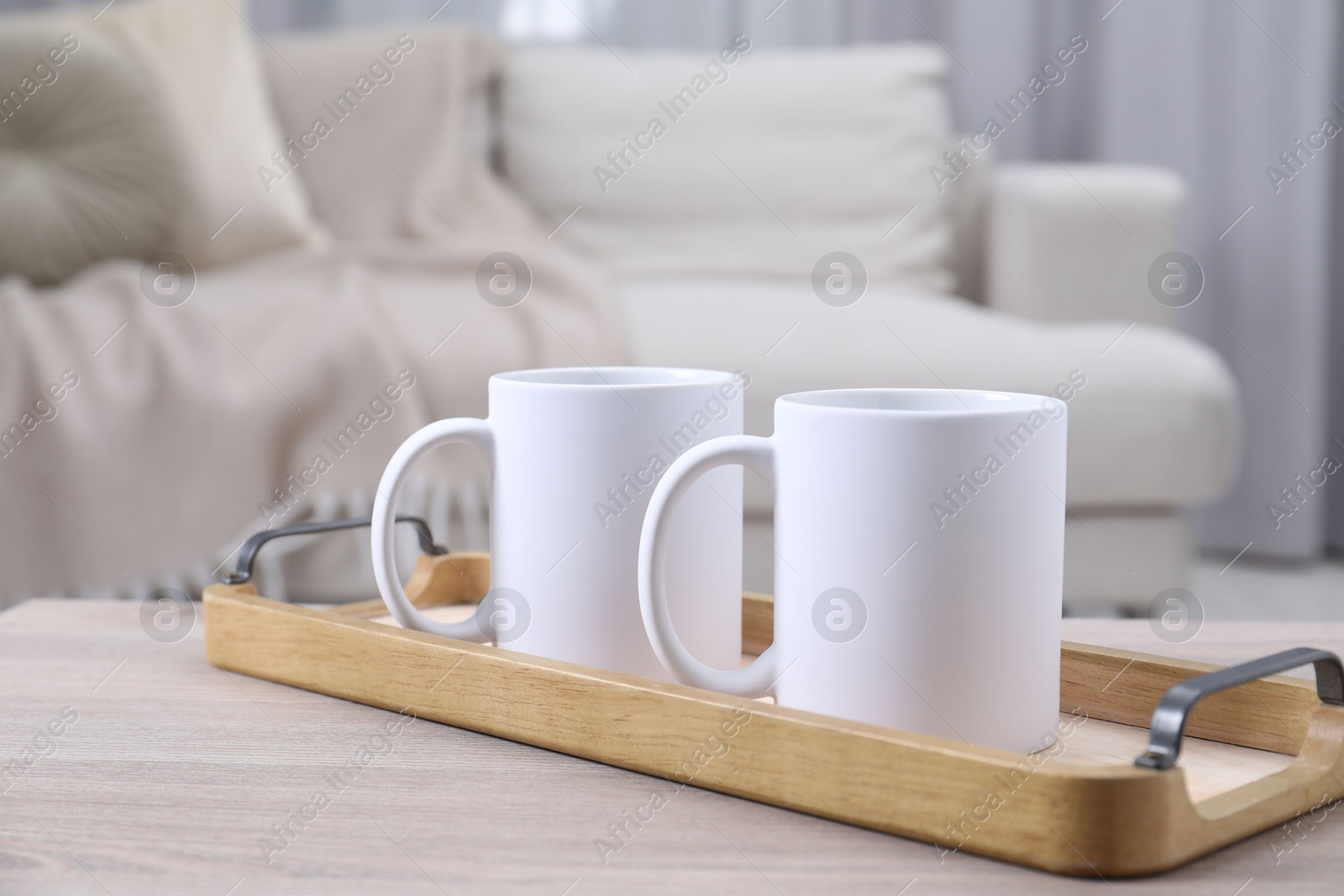 Photo of Blank ceramic mugs on white wooden table indoors. Mockup for design