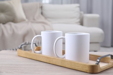 Photo of Blank ceramic mugs on white wooden table indoors. Mockup for design