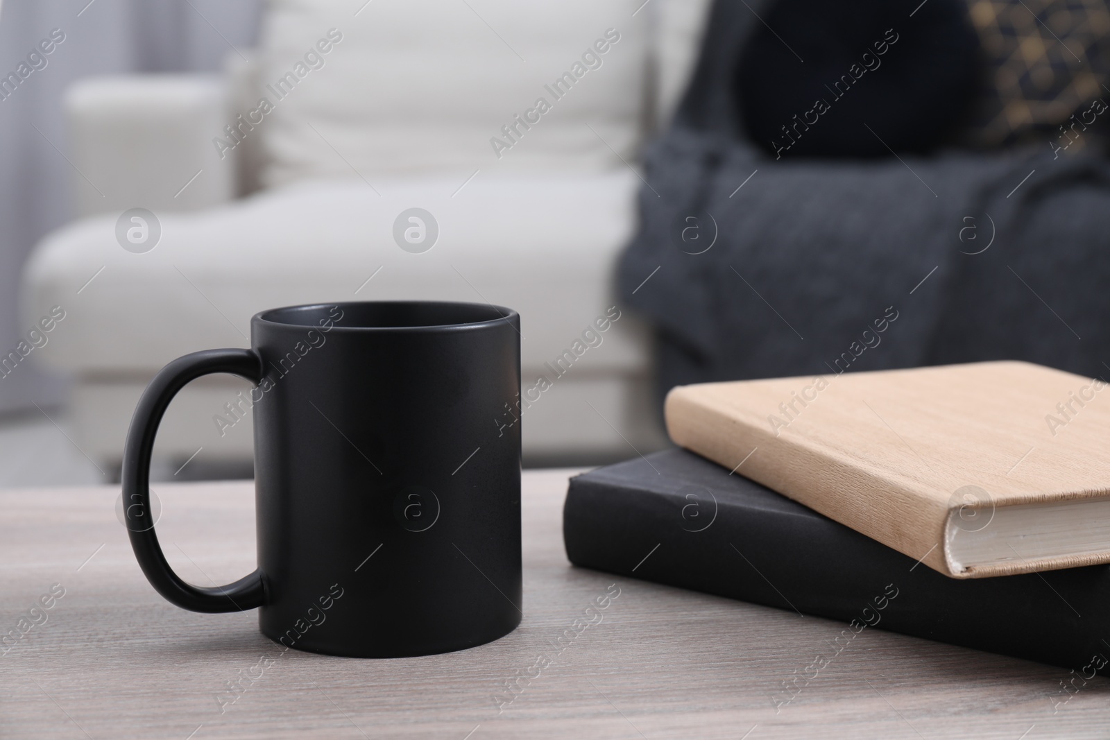 Photo of Blank black ceramic mug and notebooks on wooden table. Mockup for design