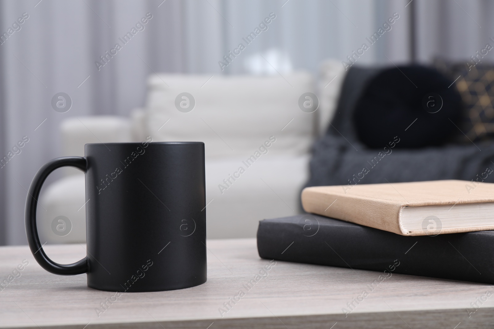 Photo of Blank black ceramic mug and notebooks on wooden table. Mockup for design