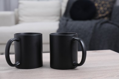 Photo of Blank black ceramic mugs on white wooden table. Mockup for design