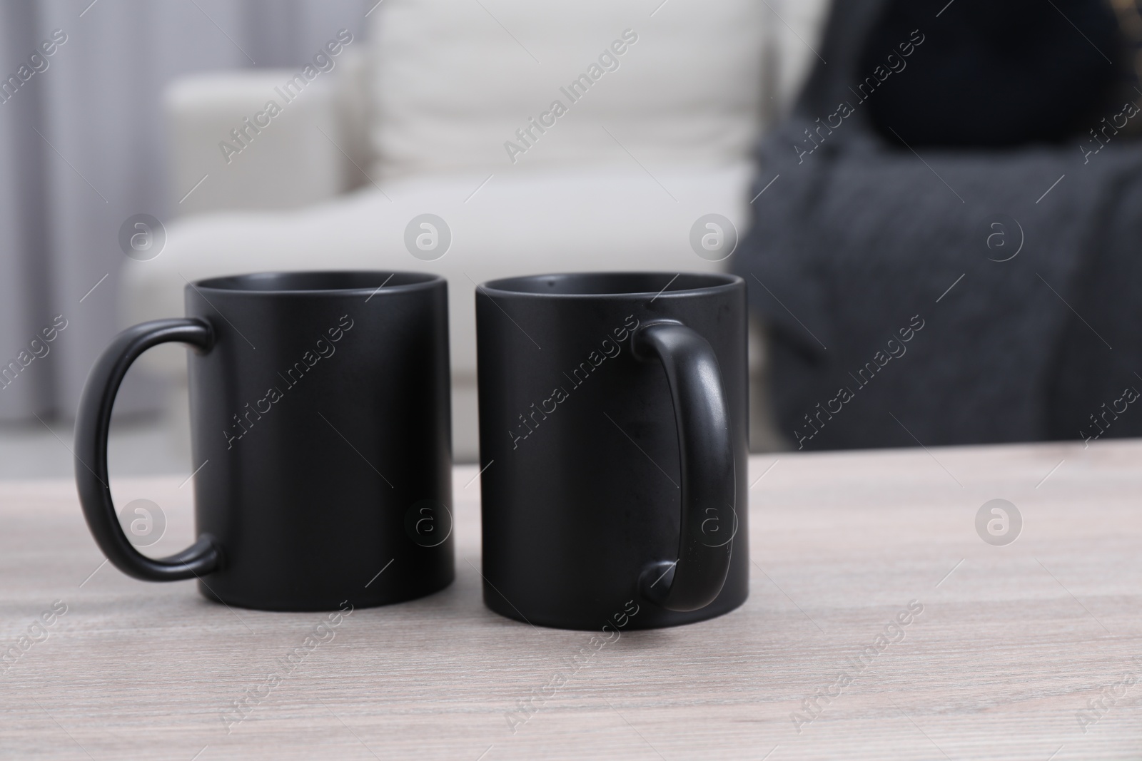 Photo of Blank black ceramic mugs on white wooden table. Mockup for design