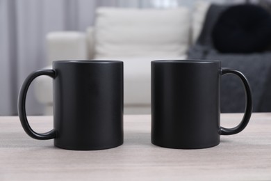 Photo of Blank black ceramic mugs on white wooden table. Mockup for design