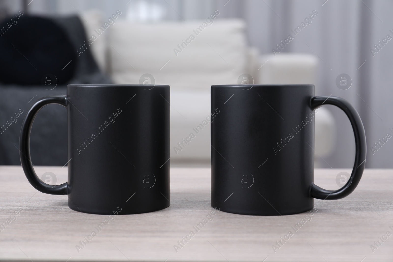 Photo of Blank black ceramic mugs on white wooden table. Mockup for design