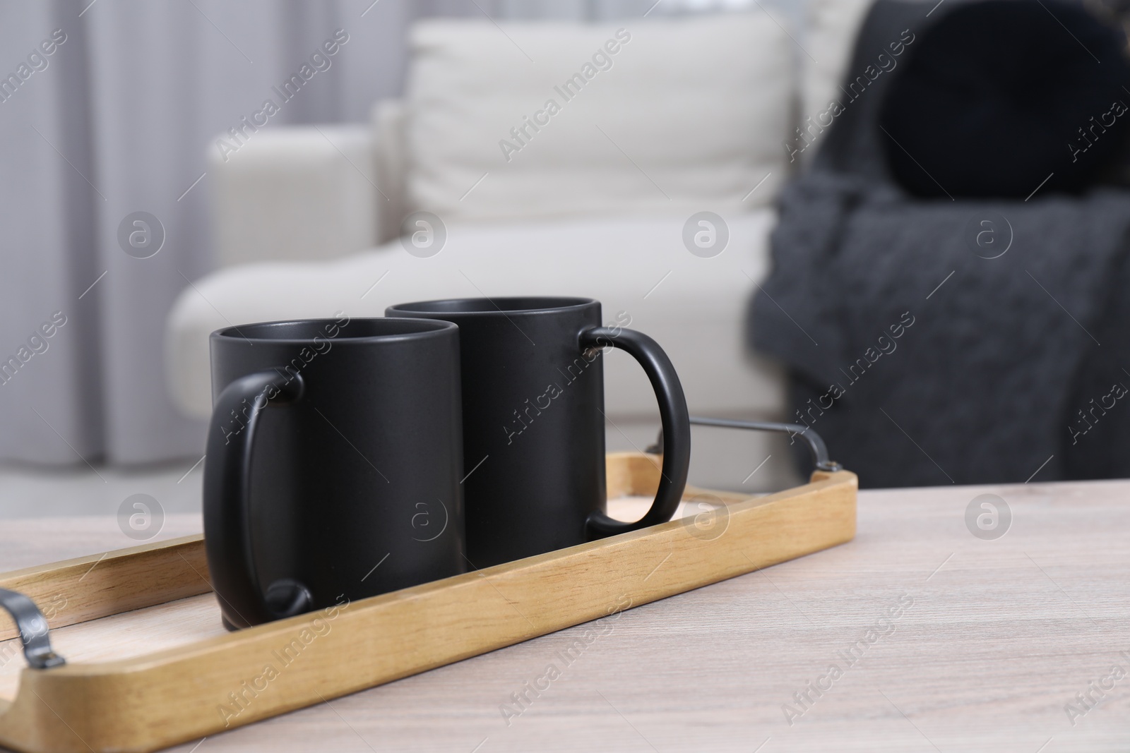 Photo of Blank black ceramic mugs on white wooden table. Mockup for design