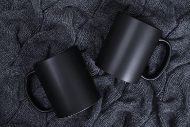 Photo of Blank ceramic mugs on black fabric, top view. Mockup for design