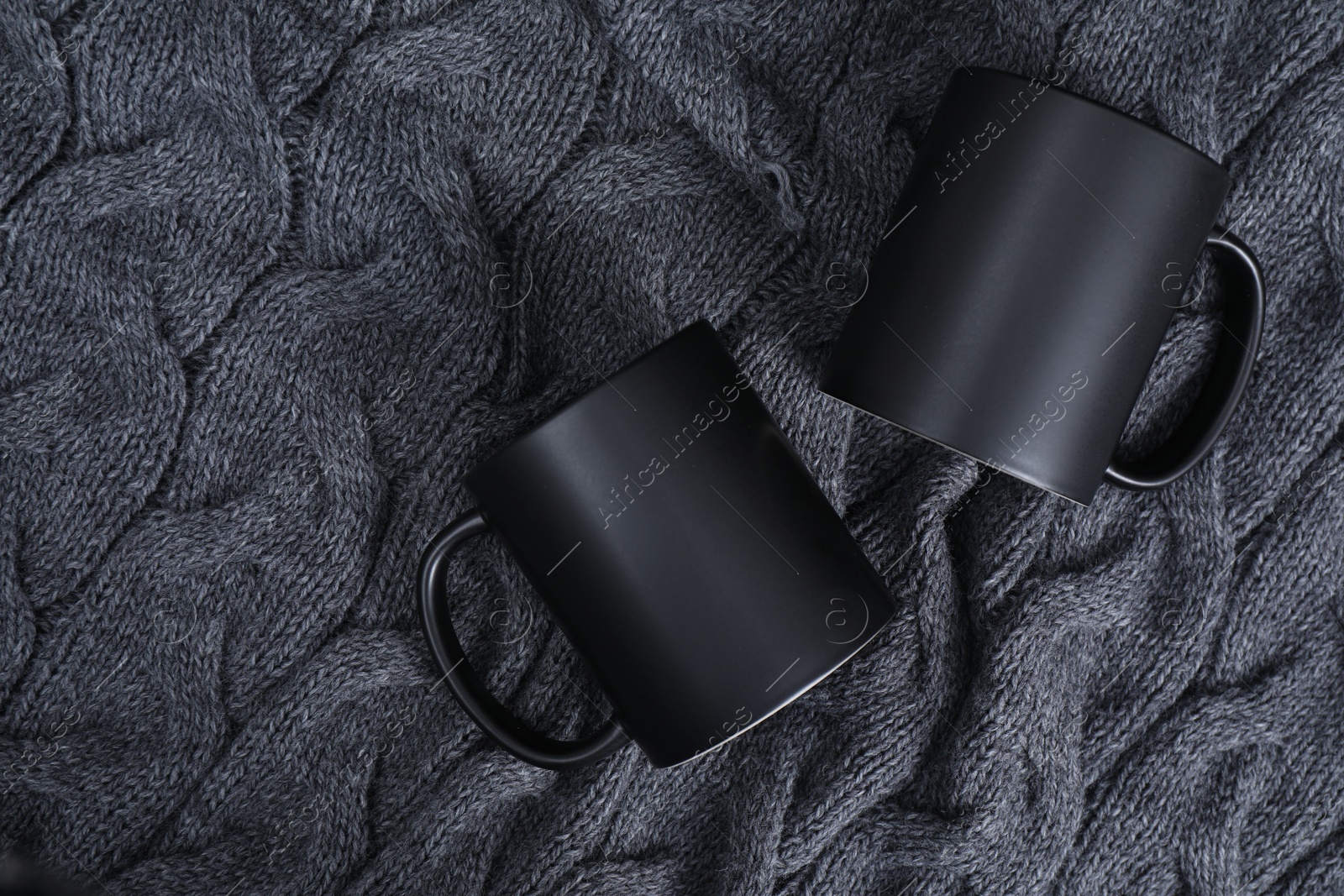 Photo of Blank ceramic mugs on black fabric, top view. Mockup for design