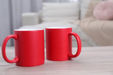 Photo of Blank red ceramic mugs on white wooden table. Mockup for design