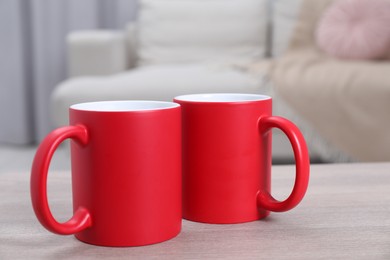 Photo of Blank red ceramic mugs on white wooden table. Mockup for design