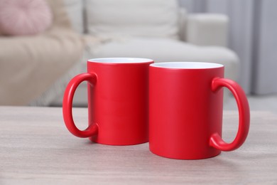 Photo of Blank red ceramic mugs on white wooden table. Mockup for design