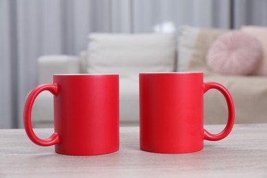 Photo of Blank red ceramic mugs on white wooden table. Mockup for design