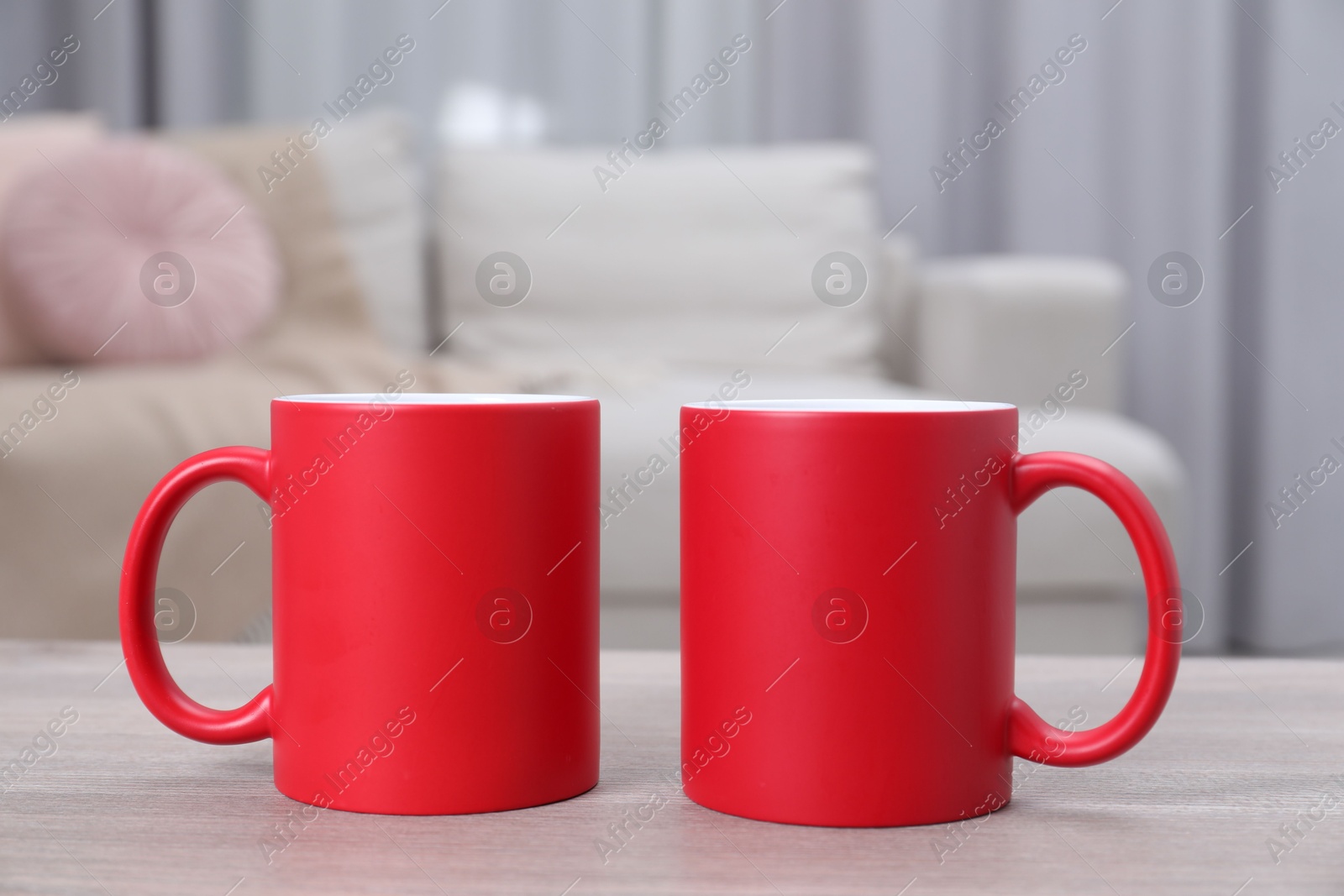 Photo of Blank red ceramic mugs on white wooden table. Mockup for design